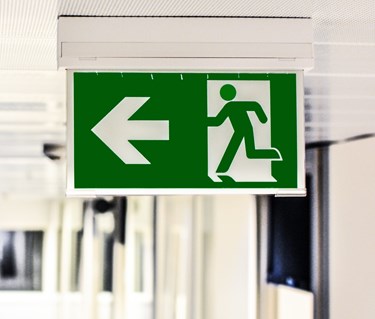 Bild på en skylt som visar en nödutgångsskylt i taket på en korridor.