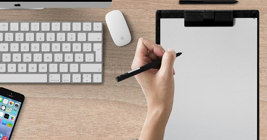 Bild som visar en skrivande hand på papper på ett skrivbord.