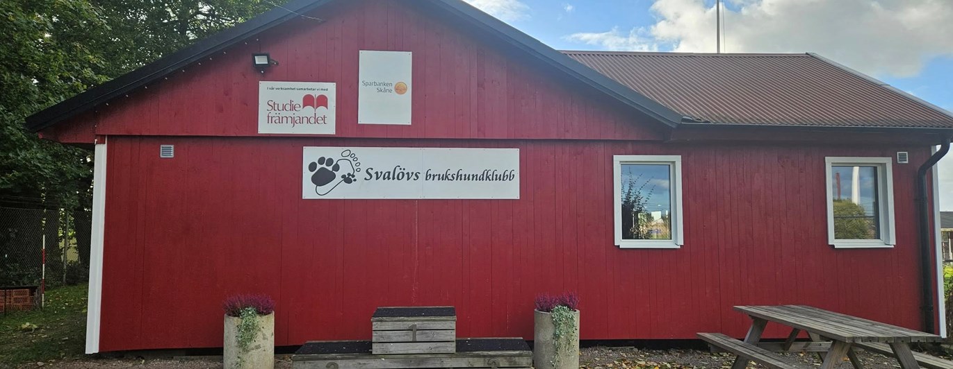 Röd klubbstuga i trä. På bilden syns också fina krukor med blommor.