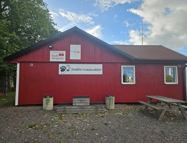 Röd klubbstuga i trä. På bilden syns också fina krukor med blommor.