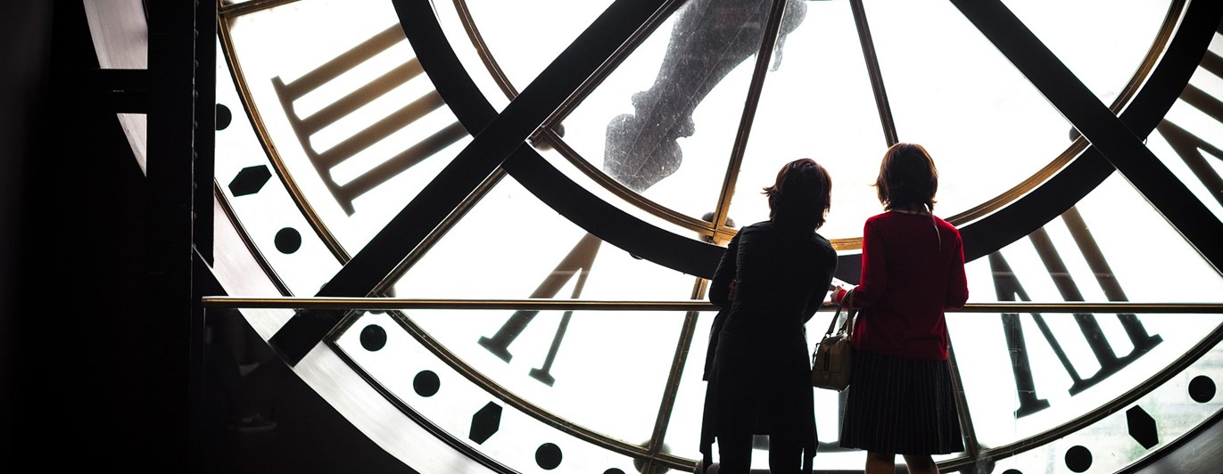 Bild som visar två kvinnosiluetter som står inuti en stor klocka.