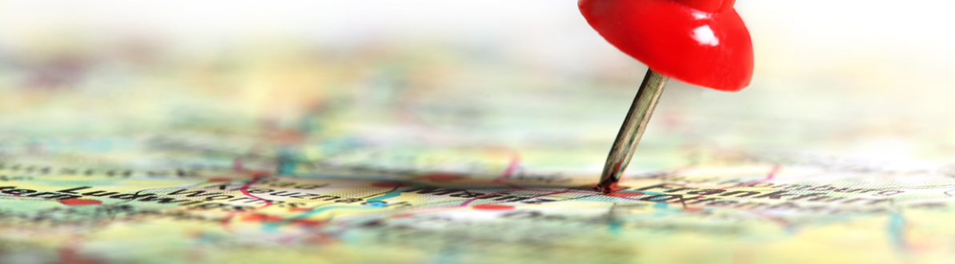 Bild med en röd nål på en karta i färg.