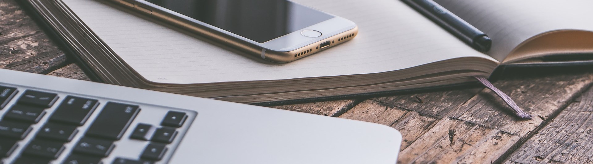 Bild som visar en bärbar dator, mobil och anteckningsblock på ett träbord.