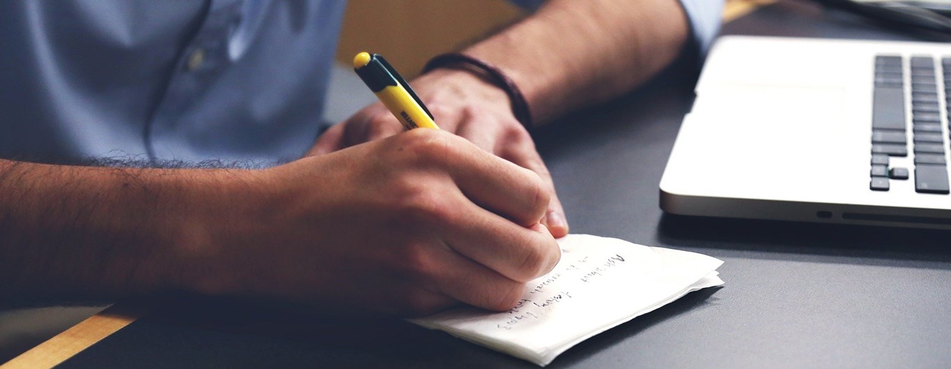 En man skriver på ett block bredvid en dator